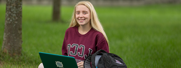 Student outside in grass with laptop